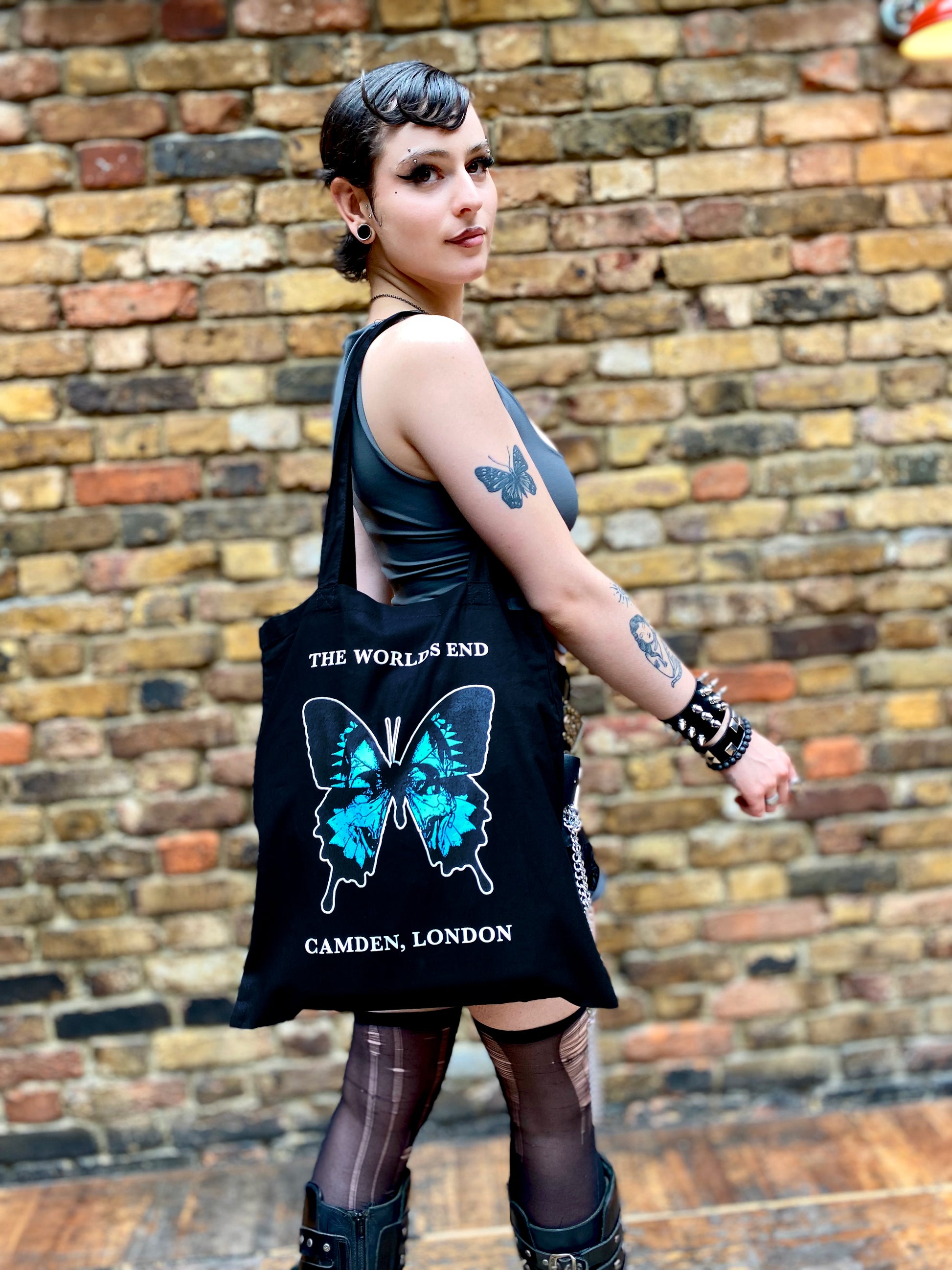 Person with the World's End Butterfly black tote bag on their shoulder.