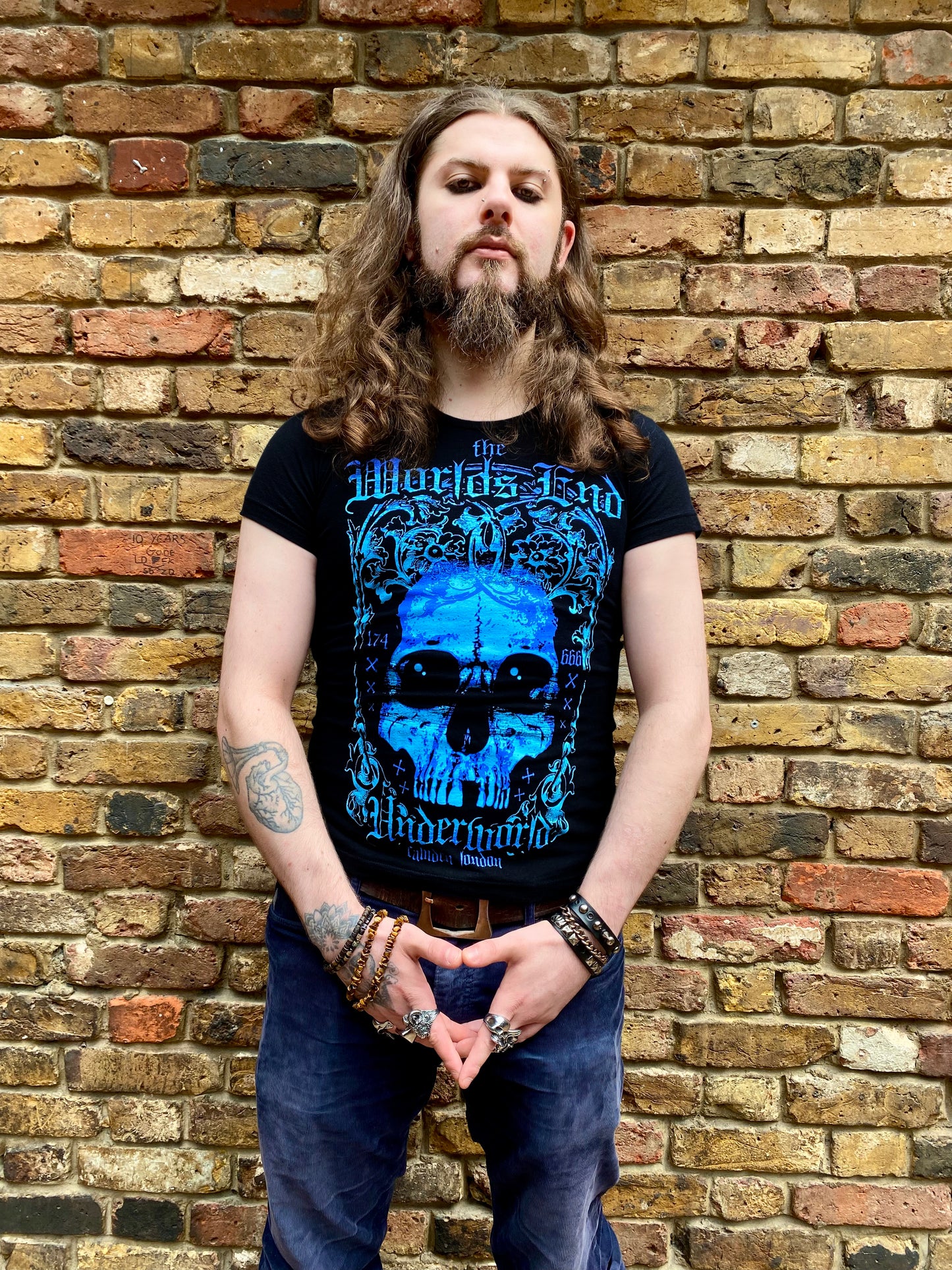 Man wearing a black t-shirt with blue graphic design against a brick wall