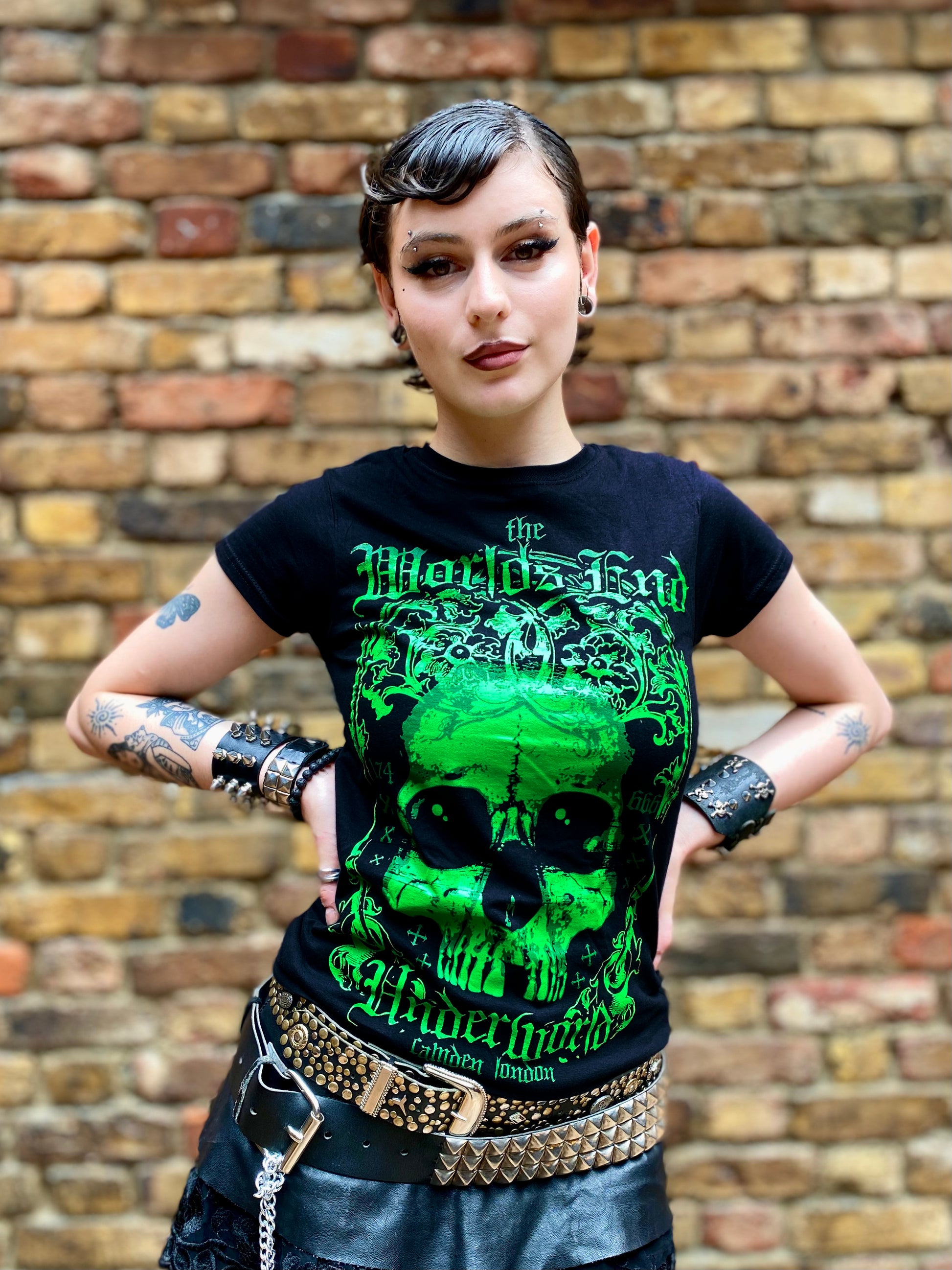 Person wearing a black t-shirt with green graphic design in front of a brick wall
