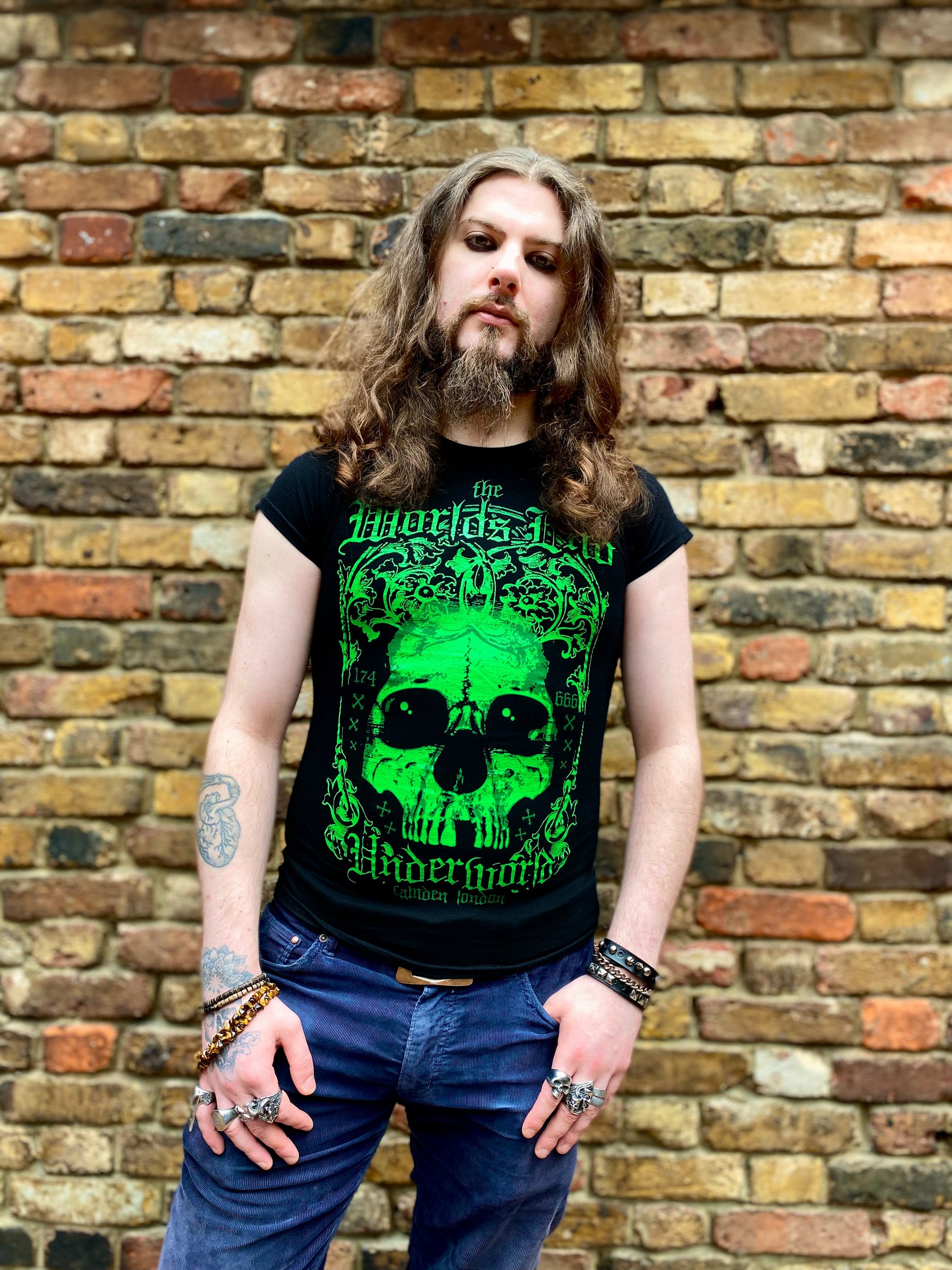 Person wearing a black t-shirt with green graphic design against a brick wall.